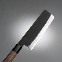 Load image into Gallery viewer, An angled shot of the Sakai Ichimonji Jo Nakiri knife, highlighting the contrast between the polished Blue Steel #2 edge and the rustic kurouchi finish.