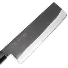 Cargar imagen en el visor de la galería, An angled shot of the Sakai Ichimonji Jo Nakiri knife, highlighting the contrast between the polished Blue Steel #2 edge and the rustic kurouchi finish.